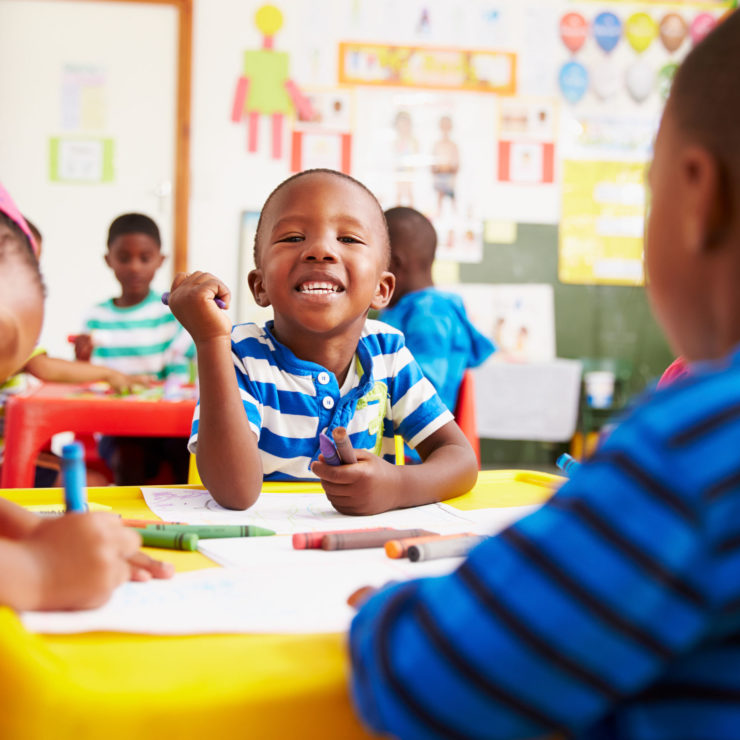 Children drawing and smiling at the camera demonstrating the power of kindness and compassion in the classroom.