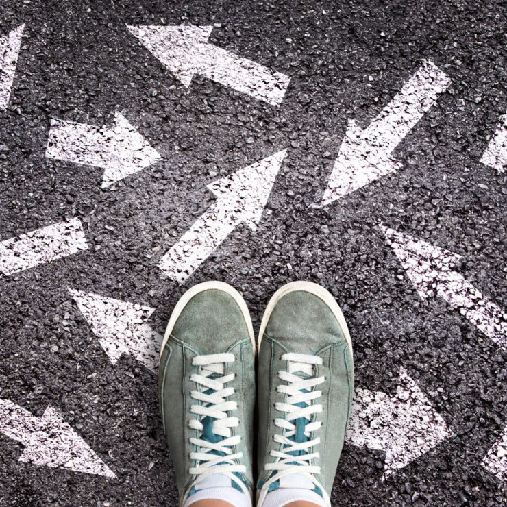 Person Standing On Pavement With Directional Arrows Pointing Around Them