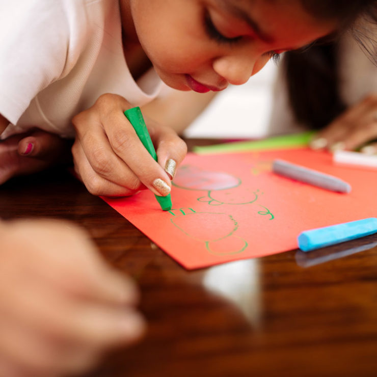 Child watching as an adult uses a green crayon to draw. This image demonstrates how adults can teach children well-being.