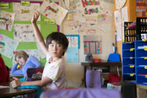 Young boy raising his hand in the classroom.