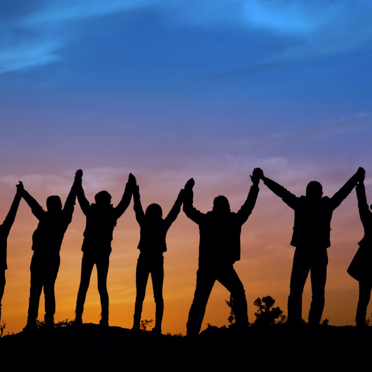 Silhouettes of youth holding hands as sun goes down. Image demonstrating teamwork and prosocial skills.