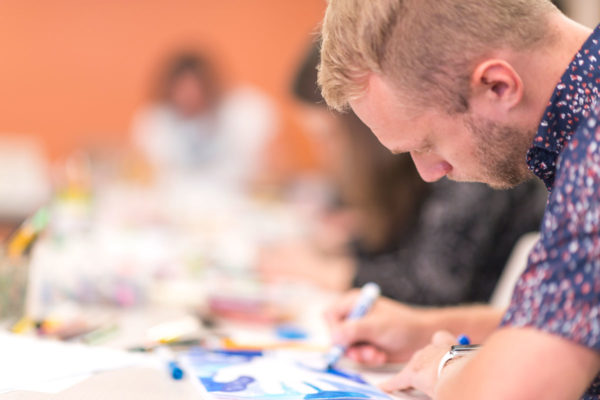 A Drawing Gym Participant Concentrates As He Draws In His Composition Notebook