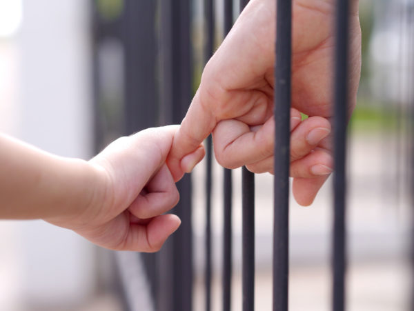 Parent And Child Linking Hands Through Bars